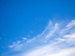 white clouds blue sky with very small floating 3 parachutes moving
