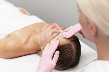 Obraz na płótnie Canvas Young beautician or dermatologist doing manual facial cleansing for a woman in a beauty salon. Spa facial massage. Beautiful woman receiving facial massage in a beauty salon. The beautician makes