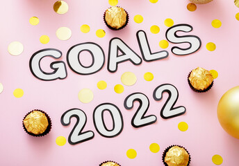 Goals 2022 lettering in Happy New Year style. 2020 Goals text with Christmas decorations gold confetti on pink color background.