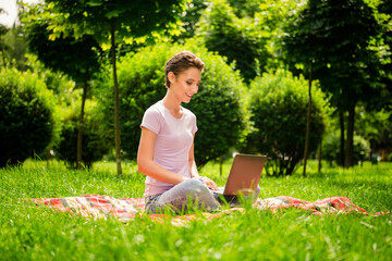 Naklejka na ściany i meble Portrait of attractive cheerful girl sitting on veil using laptop typing e-mail chatting on fresh air outdoors