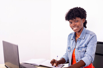 young woman taking notes using laptop computer smiling.