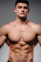 Fototapeta premium A young sexy athlete with perfect abs poses in the studio topless in jeans on the background. Healthy lifestyle, proper nutrition, training programs and nutrition for weight loss.