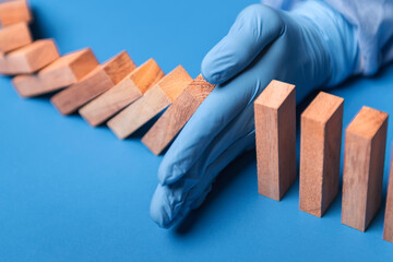 hand of doctor in medical glove stopping falling domino in a virus crisis management concept image.