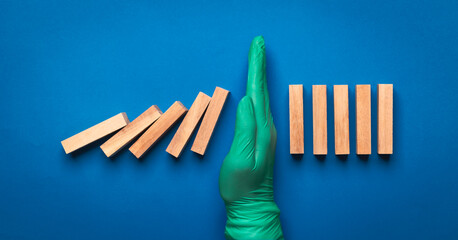 hand of doctor in medical glove stopping falling domino in a virus crisis management concept image.