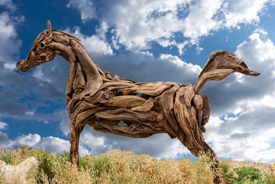 Horse made of tree roots against a blue sky with cumulus clouds.