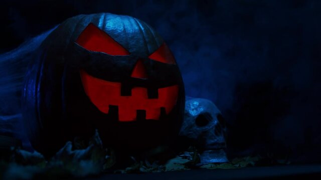 Scary laughing pumpkin and an old skull on a dark background. Halloween, witchcraft and magic.
