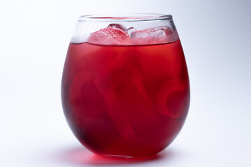 Red water with ice in a clear glass on a white background.