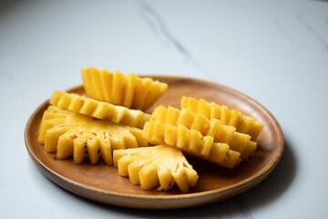 Pineapple turned slices in a wooden plate on the table.