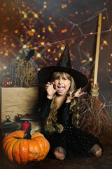 Copy space for Happy Halloween on the photo Preschool girl scares, expression of emotions evil laughter in a witch's hat with a pumpkin 