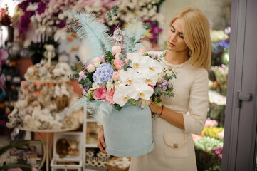 young attractive blonde woman holding in her hands box with flowers decorated with blue feathers