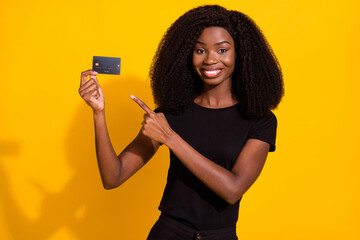 Photo of attractive happy dark skin brunette haired woman point finger credit card smile isolated on yellow color background