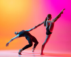 Two dancers, stylish sportive couple, male and female models dancing contemporary dance on colorful gradient yellow pink background in neon light.