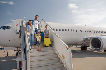 Happy family of four getting off the plane on a daytime. People, traveling, vacation concept