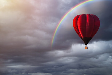 Red balloon flying under storm clouds and rainbow