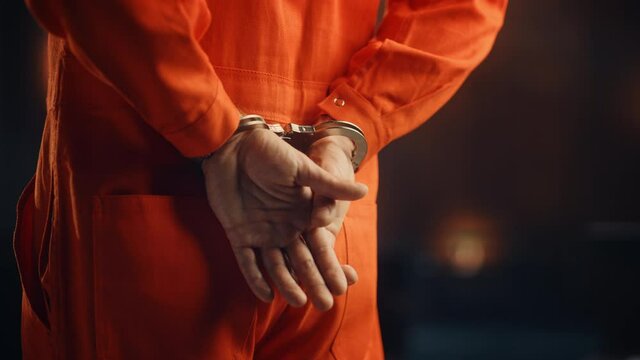 Cinematic Close Up Footage of a Handcuffed Convict at a Law and Justice Court Trial. Handcuffs on Accused Criminal in Orange Jail Jumpsuit. Law Offender Sentenced to Serve Jail Time.