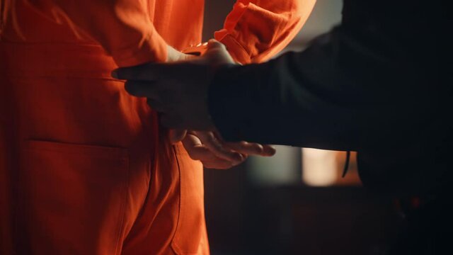 Cinematic Close Up Footage of a Policeman Handcuffing Convict at a Law and Justice Court Trial. Prison Guard Puts Handcuffs on Accused Criminal in Orange Jail Jumpsuit. Sentenced to Serve Jail Time.