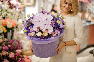Gorgeous flower arrangement in box of orchids and different purple flowers in hands of woman