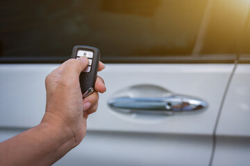 Female hand holding and pushing car remote control to lock or unlock the car.