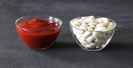 white large beans and tomato paste in glass bowls on a dark background. vegetarian food concept