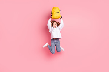 Full length body size girl jumping high keeping schoolbag over head isolated pastel pink color...