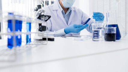 Fototapeta premium Medical or scientific researcher or man doctor looking at a test tube of clear solution in a laboratory
