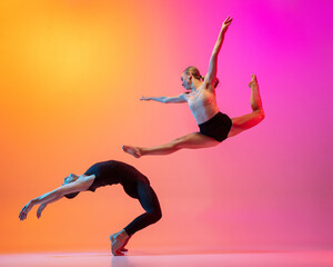 Two dancers, stylish sportive couple, male and female models dancing contemporary dance on colorful gradient yellow pink background in neon light.