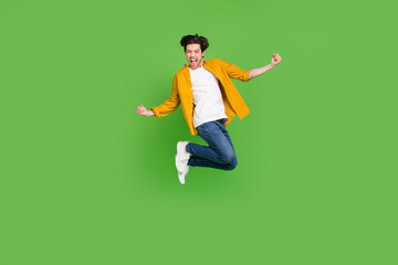 Fototapeta na wymiar Photo of cute impressed young guy dressed yellow shirt jumping high rising fists smiling isolated green color background