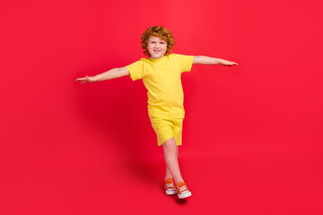 Photo of foxy carefree little boy walk raise hands balance wear yellow t-shirt isolated red color background