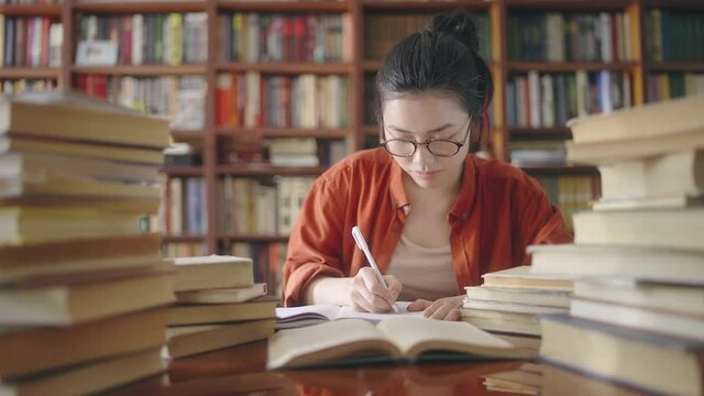 Diligent asian student writing down notes from book, writer working at library