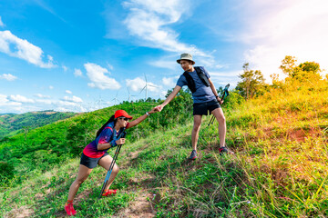 Two Asian men and women trail runners, wearing sportswear, are practicing on a high mountain behind a beautiful view of green mountains.