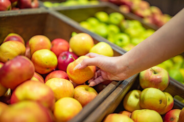Woman's hand choosing apple on fruits shelf in supermarket