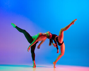 Naklejka premium Stylish sportive caucasian couple, male and female dancer dancing contemporary dance on colorful gradient blue pink background in neon light.