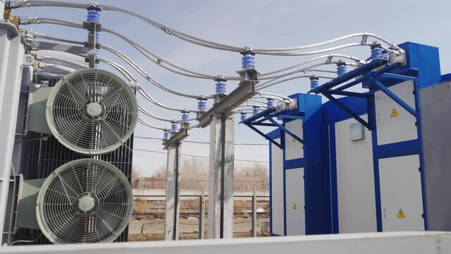 Power transformer with cables at electrical distributing substation on sunny day. Active cooling fan on modern transformer. High voltage power line on insulators.