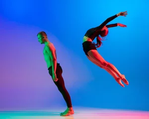 Poster Stylish sportive caucasian couple, male and female dancer dancing contemporary dance on colorful gradient blue pink background in neon light. © master1305