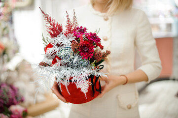 Beautiful box with flower arrangement in woman hands. Floral shop concept. Red and silver colors.