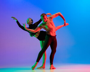 Stylish sportive caucasian couple, male and female dancer dancing contemporary dance on colorful gradient blue pink background in neon light.