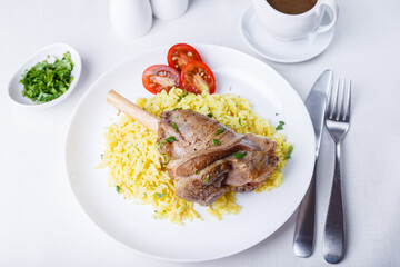 Lamb shin (shank) with rice, parsley, tomatoes and sauce on a white plate. Traditional dish. Close-up, selective focus