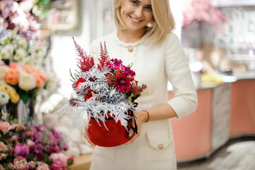pretty woman with round box of flower arrangement in her hands. Red and silver colors.