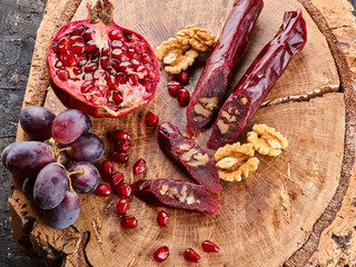 slicing Churchkhela, pomegranate, grapes and nuts on a wooden background, top view, serving