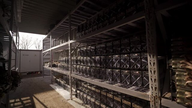 Bitcoin ASIC miners in warehouse. ASIC mining equipment on stand racks for mining cryptocurrency in steel container. Blockchain techology application specific integrated circuit units storage.