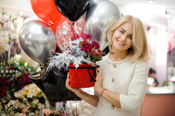 Smiling woman with round box of flower arrangement in her hands. Red and silver colors.