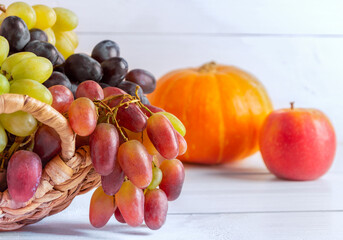 Still life with grapes in a basket, pumpkin and apple in the background. Wooden light background.