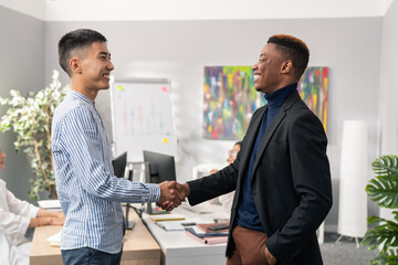 Two elegant men dressed in shirt and jacket are standing in the office of the company, smiling, shaking hands, greeting, goodbye, congratulations, thanks, expression of respect
