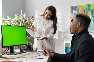 A beautiful brunette of Asian beauty dressed in a white dress comes to the men sitting in front of the computer screen designing graphics, girl shows them graphs of revenue growth guys happy smile