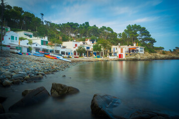 Long exposure picture of S'Alguer beach with its typical painted doors in Costa Brava. Photography of a beautiful creek in Palamós with boats and kayaks on shore.