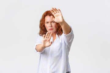Serious-looking concerned and displeased redhead middle-aged woman protecting herself, extend hands...