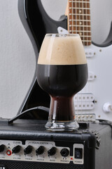 Tube combo or amplifier for guitar with black and white electric guitar and glass of dark stout beer with foam against on a white wall. Selective focus