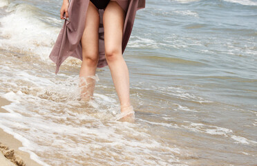 legs of a young woman standing on the sand by the sea