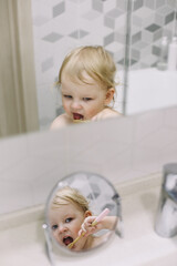 reflection in the mirror of a little funny girl brushing her teeth