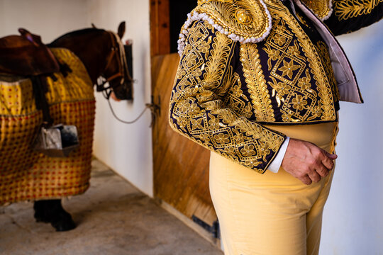 Crop bullfighter in yellow costume standing in stable